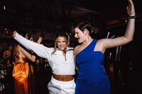 A bride dressed in white casual sweats dances at the reception with a guest