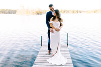 Groom on the dock standing behind his bride as he looks at her with a smile at the luxury Catalyst By Nature Link venue  | Minnesota wedding photographer