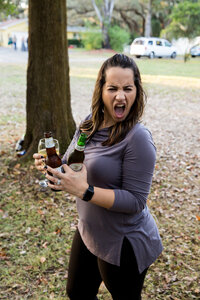 woman holding beer bottles and wine glass while making a silly face