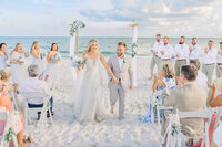 Bride and groom walking hand in hand down the sandy aisle at Pensacola Beach, celebrating their love with the ocean breeze as their witness.