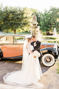 bride and groom standing in front of white old car