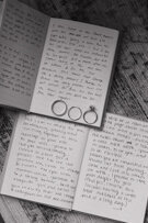 Two vow books lay spread open on a light colored rug revealing Kelsey and Connor's handwritten wedding vows to each other. Their wedding bands and Kelsey's engagement ring sit in the bottom right corner of the top vow book