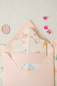 Coral, pink, and blue watercolor flowers and butterflies on a die cut Rosemary Beach save the date. The belly band has a blind embossed butterfly and monogram