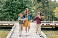 A family of two boys and a girl walk along a wooden bridge