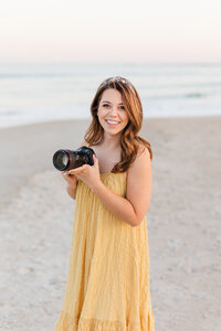 Woman in a yellow dress on a beach holding a camera