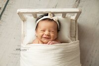 smiling newborn girl in little bed