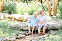 Two young siblings sitting on a rock with their barefeet in a small creek at the the