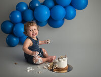 baby smashing a cake with blue balloons behind him at st. louis cake smash session