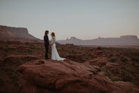 Couple stand facing each other with Castleton Tower behind them.
