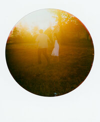 Polaroid photo of an engaged couple sharing pizza on the floor of a styled indoor set with tropical leaves and disco balls — captured by a film wedding photographer during an engagement session.