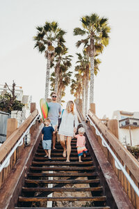 A family walks down a long flight of stairs on their way to surf during their lifestyle family photos on the beach