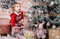 Little girl in red dress gazing up at the Christmas tree in Calini Weddings Studio – cozy festive scene with sparkling ornaments and warm tones.
