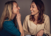 Twee lachende dames kijkend naar elkaar voor een zakelijke fotoshoot.