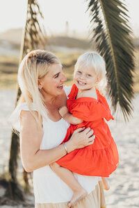 A mother holds her daughter as they laugh and smile together on the beach in front of Hotel del coronado in San Diego