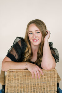 Courtney Paige smiling while leaning on the back of a chair in a studio setting.
