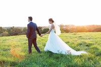 Minnesota bride  and groom in her elegant and modern wedding dress showing it off as she strolls through the field hand in hand captured by Toly Dzyuba Photography at Bavaria Downs.