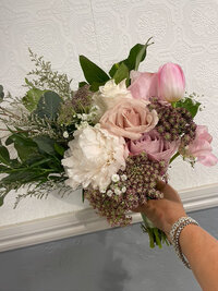 Hand holding a delicate bouquet with pastel blooms and greenery