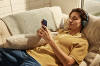 A person lounging on a cozy sofa, wearing headphones and a yellow shirt, engaged with a smartphone in a warm and inviting living room setting.