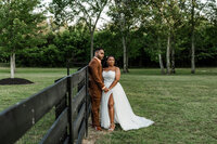 Bride and groom standing next to a fence holding hands