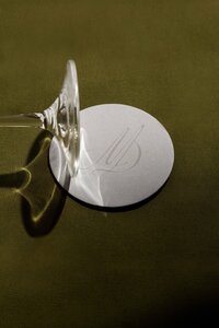 A clear wine glass is placed upside down on a white round coaster with an embossed design, set on an olive green surface—capturing the refined aesthetic perfect for Brand and Web Design for Small Businesses.
