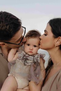 parents kissing their baby on both cheeks of the baby very sweet moment