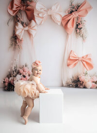 Baby girl celebrating first birthday during milestone fine art session with pink dress in La Vernia photography studio