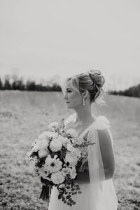 Bride in a classic A-line wedding dress holding a bouquet, styled with an elegant curly updo — timeless bridal hair by Klover Beauty in Maryland.