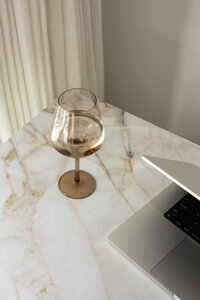 Wine glass and laptop on top of white and gold marble table