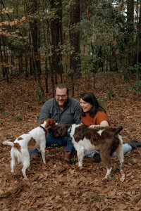 A couple crouches down to pet their two dogs in their fall colored backyard in Columbia, South Carolina.