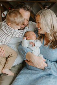 Family cuddle together on couch with toddler son and newborn son during photo session in St. Louis