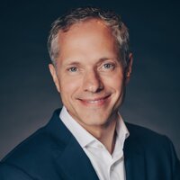 Cédric Mollaret, a white man with partially gray hair, smiles in his headshot, wearing a black suit jacket and wite shirt