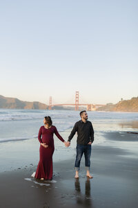man and woman standing on the beach holding hands with the golden gate bridge in the background