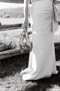 bride holding her bridal shoes standing next to a wooden fence outside
