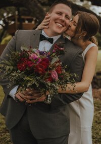 photo of newly married couple. Bride kissing groom on the cheek while groom holds her bouquet