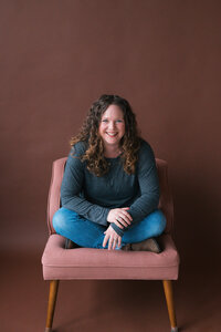 A headshot of Becky Langseth, Seattle Birth Photographer, in a studio, sitting  in a pink chair with a brown background