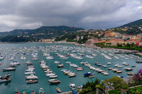 Colorful waterfront town in Lerici, Italy overlooking a marina filled with boats against a backdrop of hills and stormy skies.