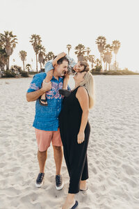 A family laughs together during their maternity photoshoot in Mission beach, San Diego