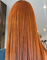Straight, vibrant copper-red hair with sleek texture, photographed under salon lighting.