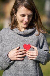 Woman wearing a turtle neck sweater holding a heart made of felt up to her chest