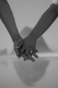 Close up black and white photo of a couple holding hands on a beach in Oregon. Behind them in the distance is Haystack Rock.