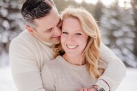 A couple smiles big while snuggling in tan sweaters in a snowy Boreas Pass