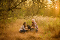 An engaged couple enjoying a sweet moment with their dog at Valley Forge National Historical Park in a rustic setting.