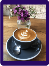 Tablet with cappuccino and foam art next to a vase with purple flowers