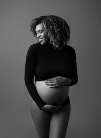 Mom in black crop top showing her baby bump and smiling. Photo taken by Jenni Nikki at the Atlanta Photography studio.