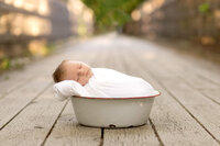 Newborn  laying in a white bucket on a bridge