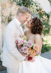 bride holding colorful wedding bouquet standing nose to nose with groom