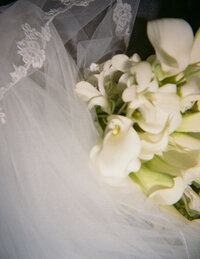 A bouquet of white calla lilies rests on a delicate lace veil. The image exudes elegance and purity, capturing a serene, bridal atmosphere.
