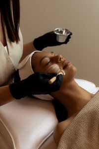 Woman receiving a calming facial treatment with natural skincare products at a wellness studio, promoting relaxation and radiant, healthy skin.