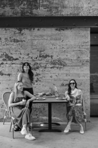 Black and white image of three women smiling and laughing outside at a bistro table