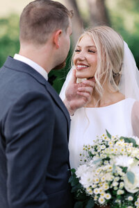 Minnesota groom gazes into his bride’s eyes while she smiles brightly and he gently holds her face during a timeless Minnesota wedding.